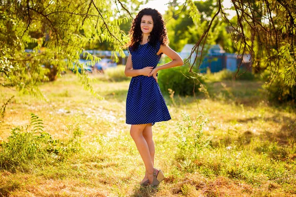 Mooie krullend vrouw poseren buiten in blauwe jurk in zonsondergang — Stockfoto