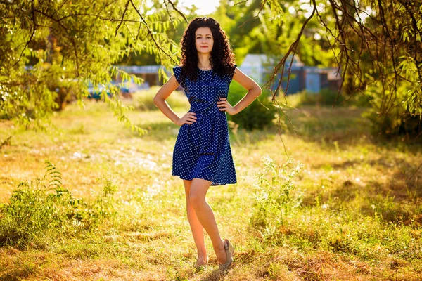 Mooie krullend vrouw poseren buiten in blauwe jurk in zonsondergang — Stockfoto