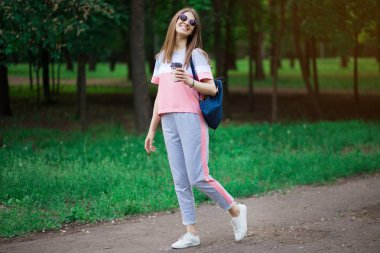 Kahve yolda. Kahve fincanı tutan ve sokakta yürürken gülümseyen güneş gözlüğü güzel genç kadın