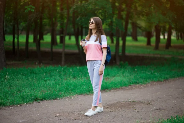 Coffee on go. Beautiful young woman in sunglasses holding coffee cup and smiling while walking along the street