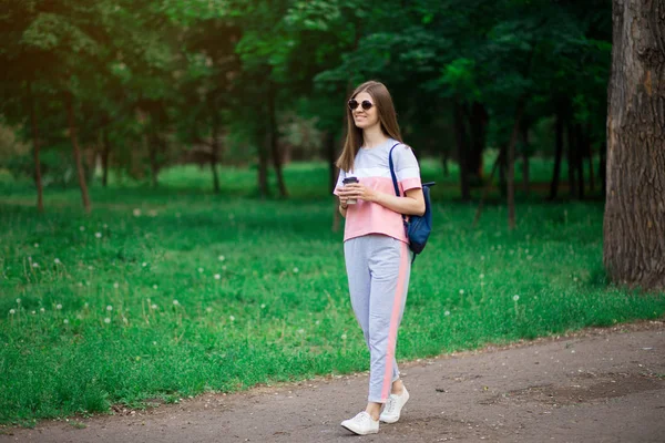 Mooie student meisje in zonnebril drinken koffie in zomerpark — Stockfoto