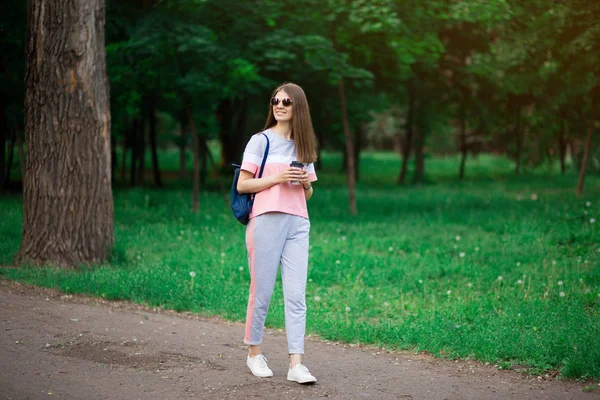 Mooie student meisje in zonnebril drinken koffie in zomerpark — Stockfoto