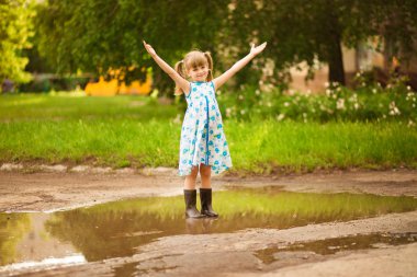 Küçük küçük kız su birikintisi boyunca koşar. yaz açık