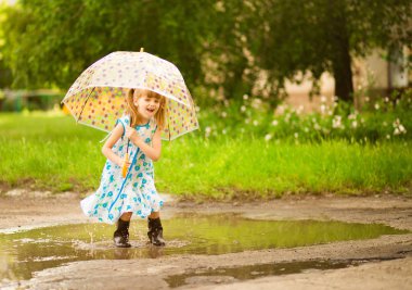 Şemsiye kauçuk çizmeler ve polka nokta elbise ve gülerek su birikintileri üzerinde atlama ile Mutlu komik çocuk kız