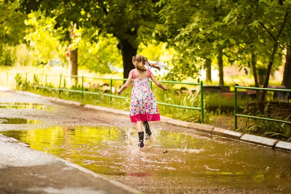 Ένα μικρό κοριτσάκι περνάει μέσα από μια λακκούβα. καλοκαίρι εξωτερική — Φωτογραφία Αρχείου