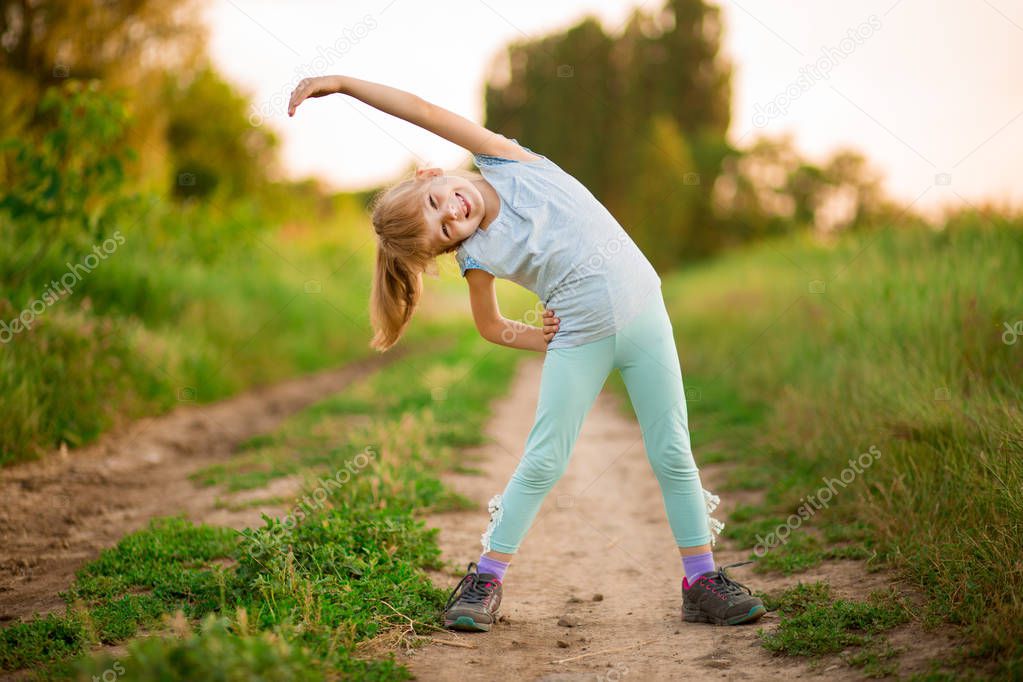 Little girl doing fitness exercises outdoor at surise