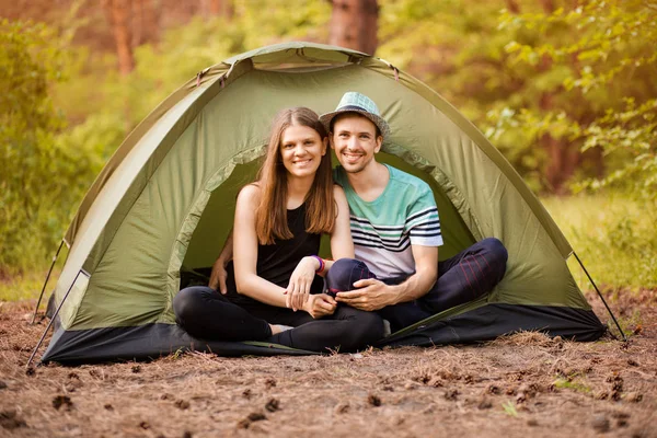 Romantic couple camping outdoors and sitting in tent. Happy Man and woman on romantic camping vacation.