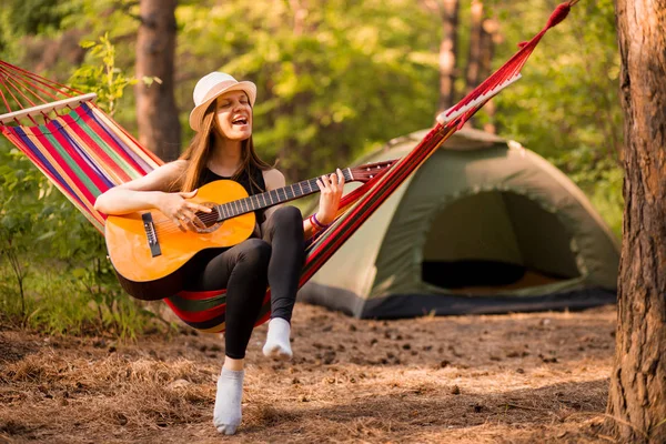 Mujer en sombrero tocar la guitarra y relajarse en hamaca en medio del bosque. Concepto de vida lenta. Hipster. . — Foto de Stock