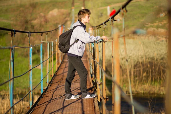 Traveling man crossing through hanging bridge in good sunny day over the river