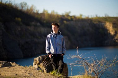 Genç bir adam göl kıyısındaki kayanın üzerinde durup ufka bakıyor. Geleceğe güvenerek