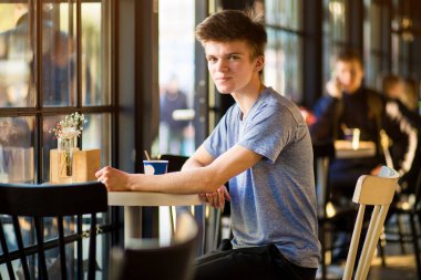 Gülümseyen Adam sıcak kahve bir fincan içme, kalabalık açık kafe.