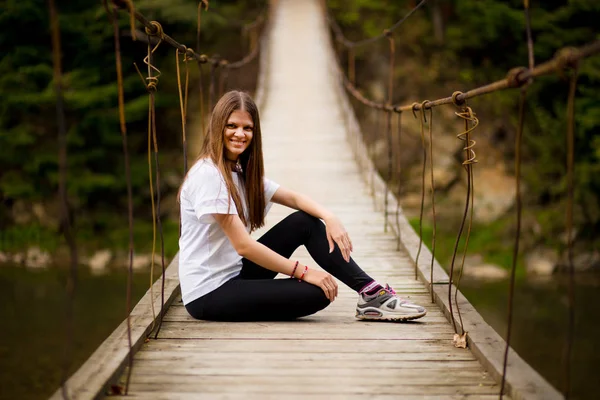 Toeristische vrouw lopen door lange houten hangbrug boven rivier. — Stockfoto