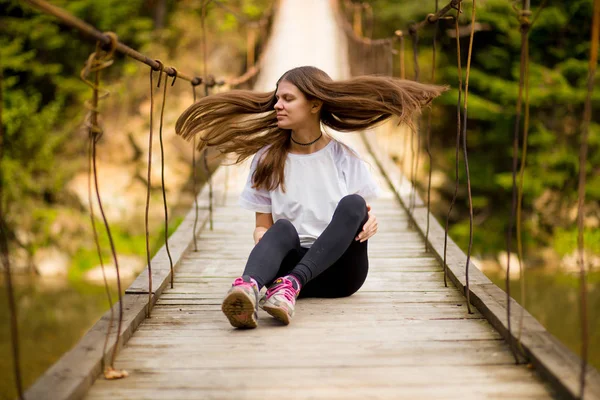 Toeristische vrouw lopen door lange houten hangbrug boven rivier. — Stockfoto