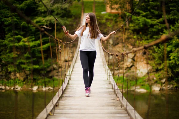 Toeristische vrouw lopen door lange houten hangbrug boven rivier. — Stockfoto