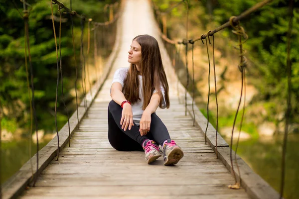 Toeristische vrouw lopen door lange houten hangbrug boven rivier. — Stockfoto