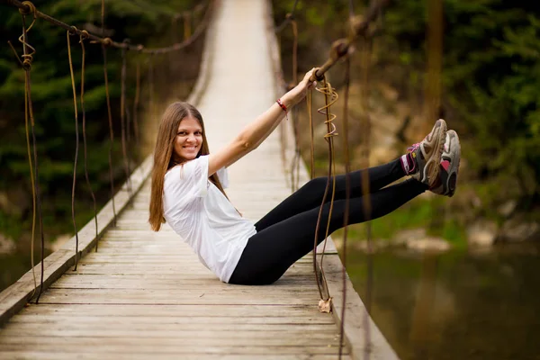 Toeristische vrouw lopen door lange houten hangbrug boven rivier. — Stockfoto