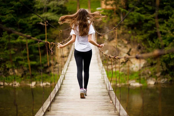 Turista mujer caminar por largo puente colgante de madera sobre el río . —  Fotos de Stock