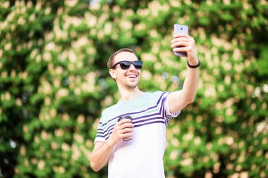 Cep telefonu açık havada bakarak kahve fincan ile güneş gözlüğü cutie adam