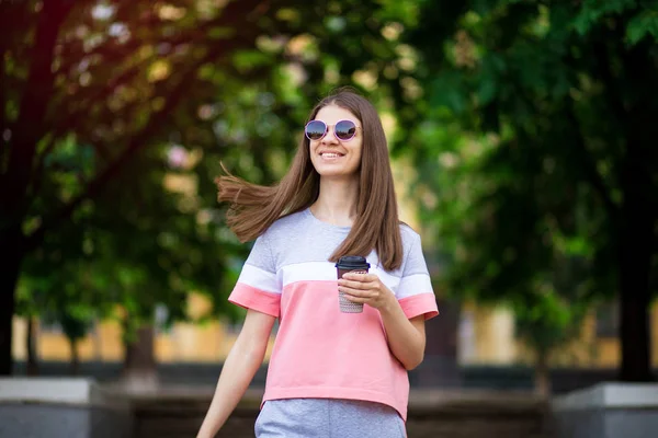 Belle fille en lunettes de soleil marcher dans la rue d'été avec du café. Concept de style de vie — Photo