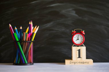 Kavram okula geri döndü. Siyah tahta arka plan üzerinde 1 Eylül'de ayarlanmış renkli kalemler ve ahşap takvim ile Re çalar saat. Kopyalama alanı malzemeleri tasarla