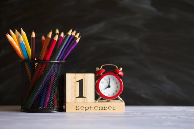 Kavram okula geri döndü. Siyah tahta arka plan üzerinde 1 Eylül'de ayarlanmış renkli kalemler ve ahşap takvim ile Re çalar saat. Kopyalama alanı malzemeleri tasarla