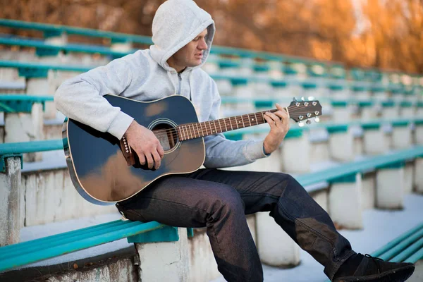 Joven sentado en los escalones tocando la guitarra y cantando, concepto musical — Foto de Stock