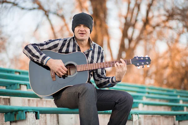 Joven sentado en los escalones tocando la guitarra y cantando, concepto musical — Foto de Stock