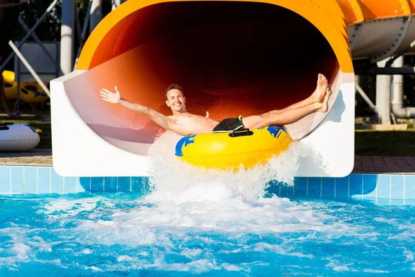 Grappig opgewonden man genieten van zomer vakantie in waterpark paardrijden gele float lachen. — Stockfoto