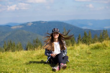 Dağın tepesinde oturan genç kadın, alçak sabah bulutlarını ve sakin gün doğumuna huzur içinde bakıyor.