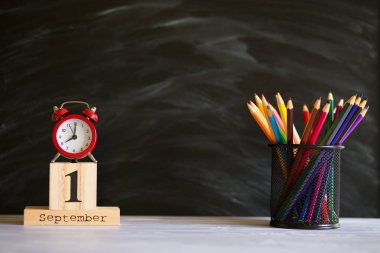 Kavram okula geri döndü. Siyah tahta arka plan üzerinde 1 Eylül'de ayarlanmış renkli kalemler ve ahşap takvim ile Re çalar saat. Kopyalama alanı malzemeleri tasarla