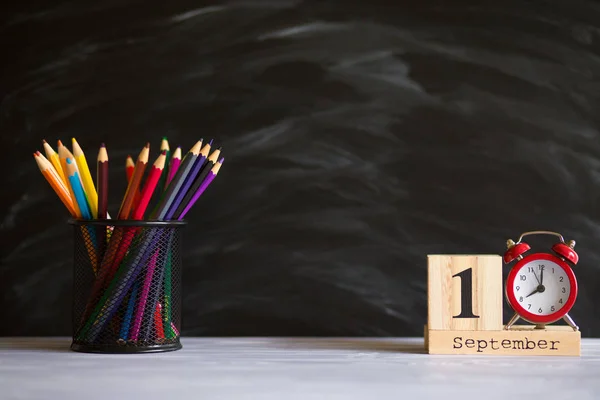 Concept terug naar school. Re wekker met kleurpotloden en houten kalender ingesteld op 1 september op zwarte Blackboard achtergrond. Ontwerp kopie ruimte benodigdheden — Stockfoto