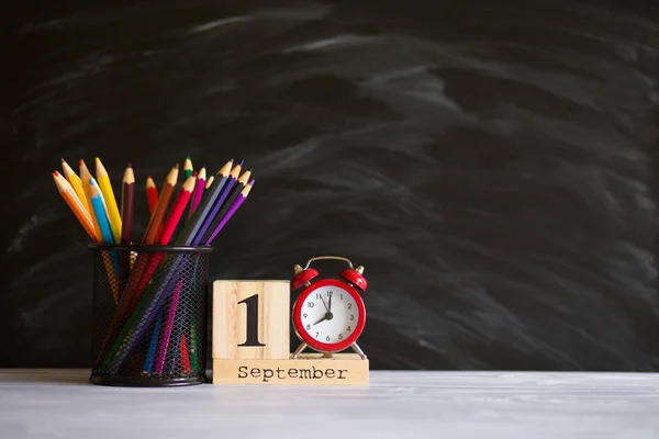 Concept terug naar school. Re wekker met kleurpotloden en houten kalender ingesteld op 1 september op zwarte Blackboard achtergrond. Ontwerp kopie ruimte benodigdheden — Stockfoto