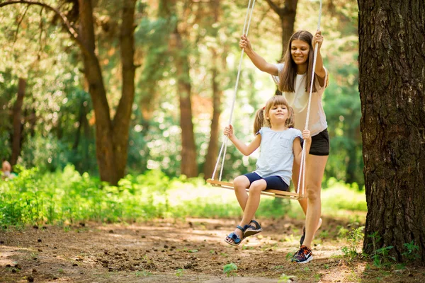 Ευτυχισμένη μητέρα πιέζει το γέλιο κόρη σε swing σε ένα πάρκο — Φωτογραφία Αρχείου
