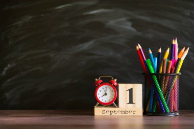 Kavram okula geri döndü. Siyah tahta arka plan üzerinde 1 Eylül'de ayarlanmış renkli kalemler ve ahşap takvim ile Re çalar saat. Kopyalama alanı malzemeleri tasarla