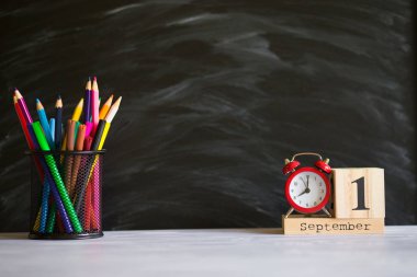 Kavram okula geri döndü. Siyah tahta arka plan üzerinde 1 Eylül'de ayarlanmış renkli kalemler ve ahşap takvim ile Re çalar saat. Kopyalama alanı malzemeleri tasarla