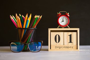 Kavram okula geri döndü. Siyah tahta arka plan üzerinde 1 Eylül'de ayarlanmış renkli kalemler ve ahşap takvim ile Re çalar saat. Kopyalama alanı malzemeleri tasarla