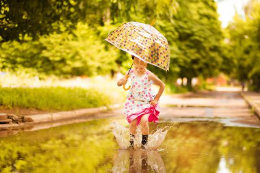 Şemsiye kauçuk çizmeler ve polka nokta elbise ve gülerek su birikintileri üzerinde atlama ile Mutlu komik çocuk kız