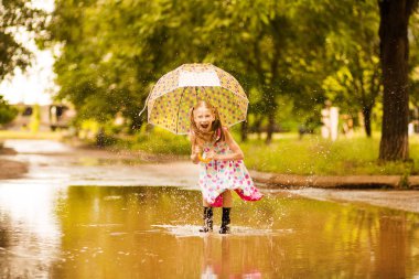 Şemsiye kauçuk çizmeler ve polka nokta elbise ve gülerek su birikintileri üzerinde atlama ile Mutlu komik çocuk kız