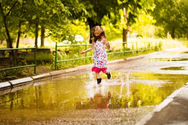 Küçük küçük kız su birikintisi boyunca koşar. yaz açık