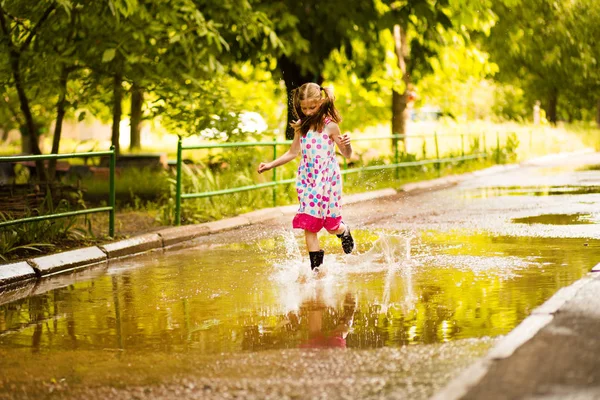 Küçük küçük kız su birikintisi boyunca koşar. yaz açık