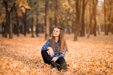 Sonbaharda mutlu kadın çim üzerinde oturur ve neşeli sarı yaprakları kadar çevirir. küçük şeyler mutluluk