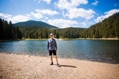 Şapkalı adam dışarıda yürüyor. Seyahat tarzı tatil kavramı. Arka planda dağ ve göl var.
