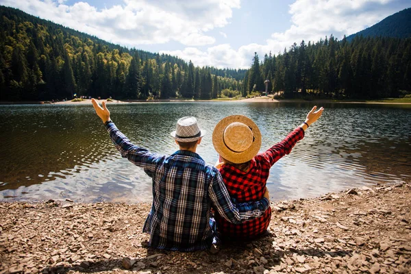 Pareja de turistas en sombrero levantando brazos y con vistas al lago turquesa y admirar la vista de las montañas — Foto de Stock