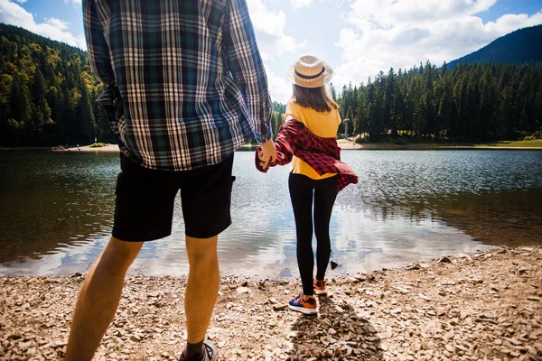 Concepto de vacaciones. Dos excursionistas en las montañas disfrutando de una hermosa vista del valle con lago y clima cálido soleado en verano, árboles verdes alrededor, el amor está en el aire — Foto de Stock