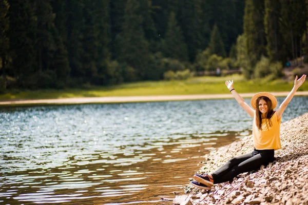 Libertad. Feliz joven sentada en la playa del lago del bosque con los brazos levantados, al aire libre . — Foto de Stock