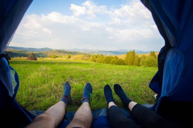 Çadırda yatan iki kişi, içeriden manzaraya batmış. Dağların güzel manzarası ile çift kamp