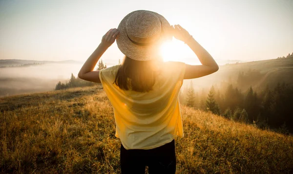 Back view of woman in straw hat stay outdoor under sunlight of sunrise with beautiful view of forest mountains — Stock Photo, Image