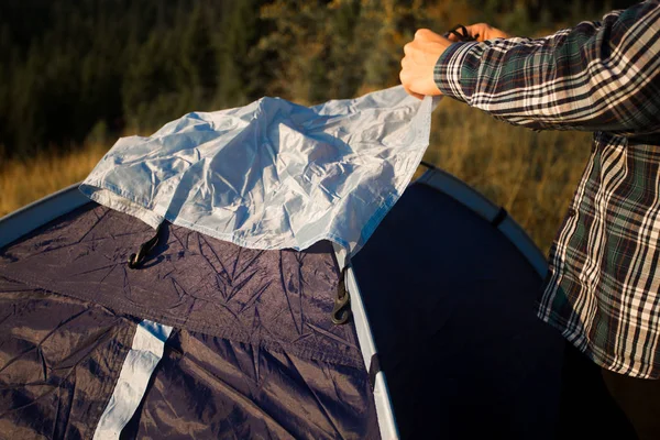 Jovem turista montando tenda no prado do outono, viajando no alto das montanhas durante o pôr do sol — Fotografia de Stock