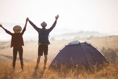 Sevgi dolu çiftin silueti sonbahar tatilinde kamp kurarak rahatlar. Moutain'in üstünde. Eller yukarı ile birlikte gün doğumunun tadını çıkarın.