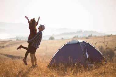Sevgi dolu çiftin silueti sonbahar tatilinde kamp kurarak rahatlar. Moutain'in üstünde. Eller yukarı ile birlikte gün doğumunun tadını çıkarın.